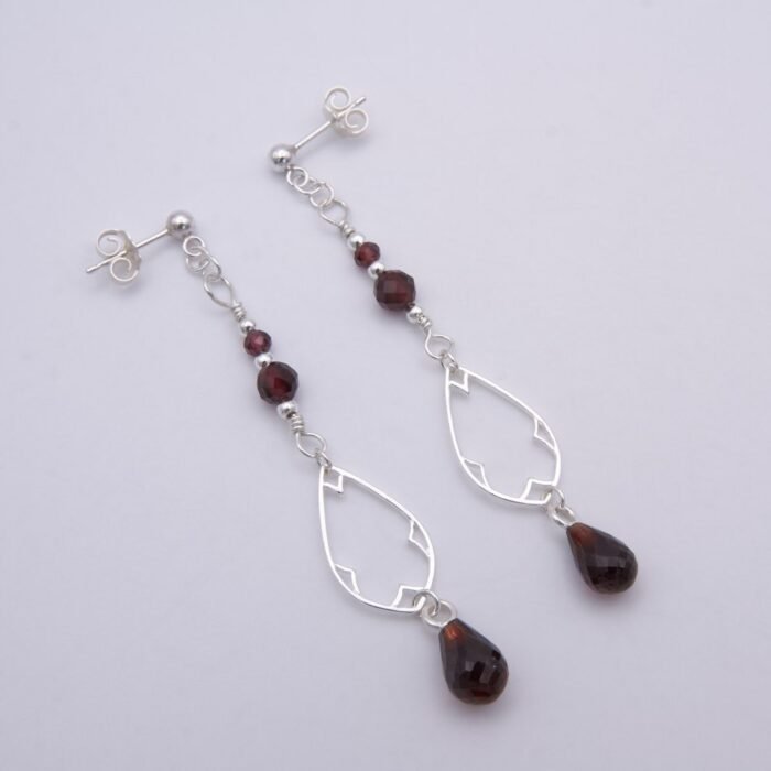 Garnet and Sterling Silver Deco Style Dangle Earrings Garnet and Sterling Silver Deco Style Dangle Earrings laid flat on white surface