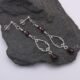 Garnet and Sterling Silver Deco Style Dangle Earrings Garnet and Sterling Silver Deco Style Dangle Earrings with two smaller garnets and silver beads at the top, a Deco style silver teardrop frame below, and a teardrop shaped garnet suspended below the frame, shown laid flat on a dark grey stone