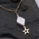 A handmade necklace featuring a diamond-shaped baroque freshwater pearl, cubic zirconia bead and gold filled star. The freshwater pearl is ivory with a pearlescent lustre and displays a variety of colours as it catches the light. Beneath the pearl is suspended a gold filled open star. A faceted round white cubic zirconia stone sits above, together with a 2mm smooth round gold filled bead. This is suspended from a gold filled satellite chain with sterling silver beads spaced evenly all around the chain. Image shows close-up of diamond and star with partial view of chain, on a dark stone background.