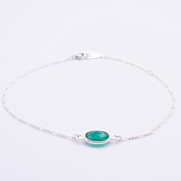 A Sterling Silver bracelet with a bezel-set Green Onyx oval faceted stone, laid flat on white surface with focus on the gemstone