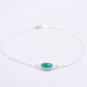 A Sterling Silver bracelet with a bezel-set Green Onyx oval faceted stone, laid flat on white surface with focus on the gemstone