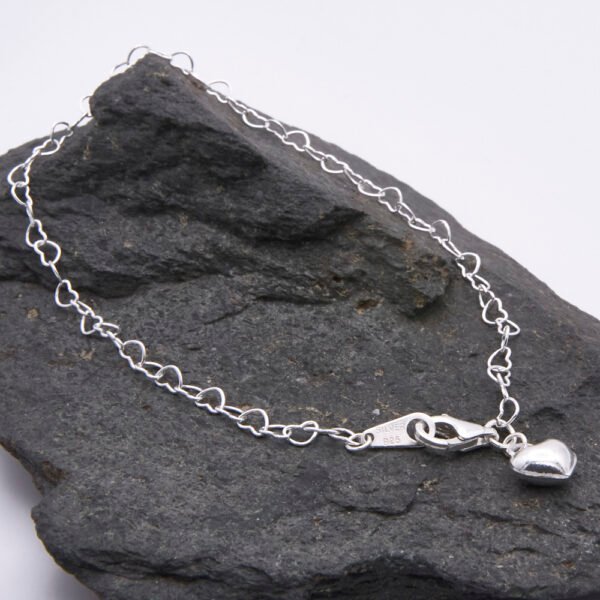 Sterling Silver Heart Link Chain Bracelet with single puffy style Sterling Silver Heart Charm fixed close to lobster clasp, shown on grey stone