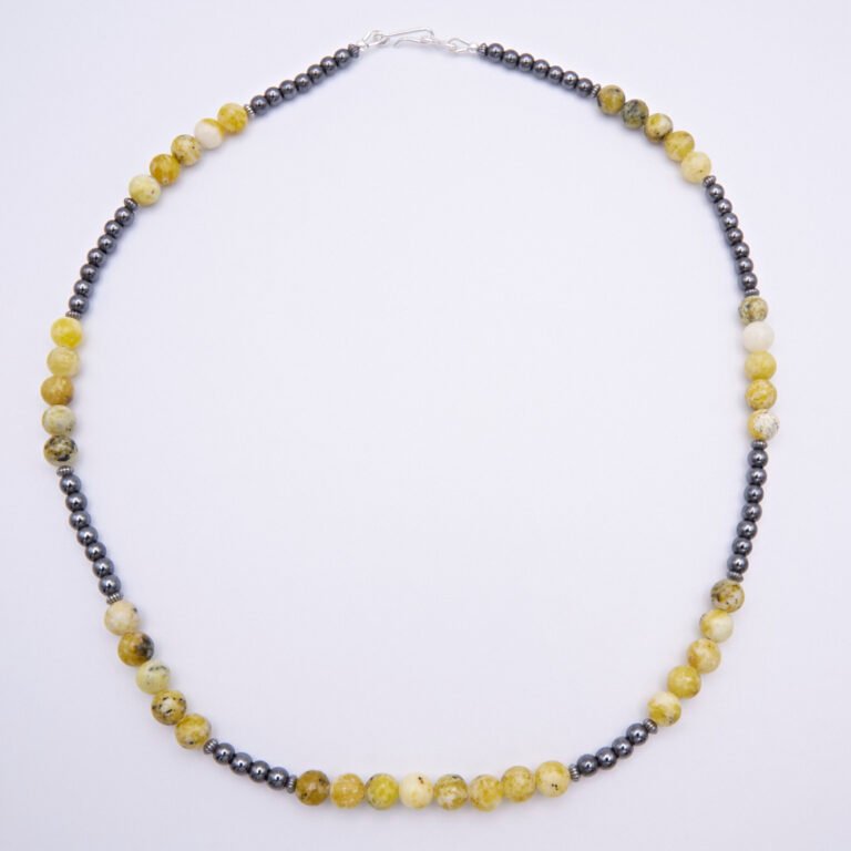 Yellow Turquoise and Hematite Sterling Silver Necklace with smooth round 6mm Yellow Turquoise beads and smooth round 3mm Hematite beads, punctuated with oxidised sterling silver corrugated saucer beads and finished with a Sterling Silver hook and eye clasp, top down view lying flat on plain white surface