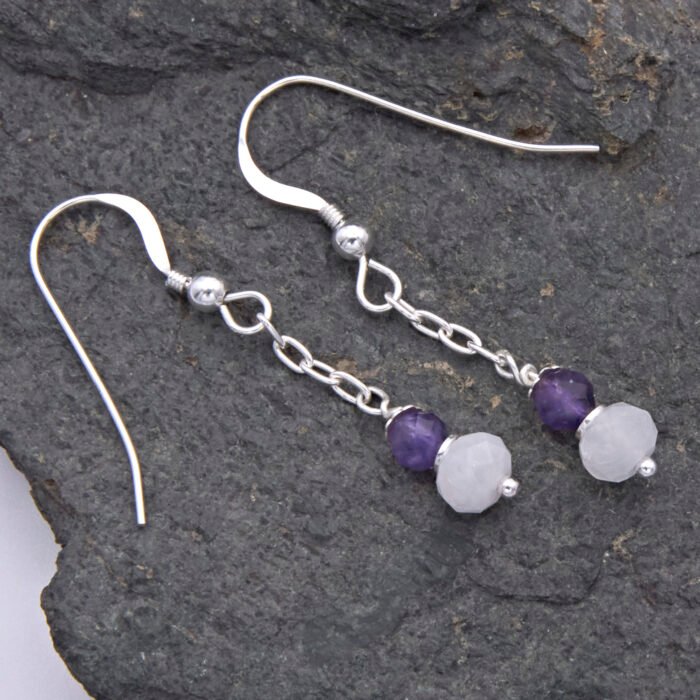 Amethyst and Rainbow Moonstone Sterling Silver Dangle Earrings laid flat on dark grey stone