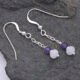 Amethyst and Rainbow Moonstone Sterling Silver Dangle Earrings laid flat on dark grey stone