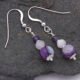 Purple Banded Agate, Rainbow Moonstone and Amethyst Sterling Silver Drop Earrings Purple Banded Agate, Rainbow Moonstone and Amethyst Stack Drop Earrings with Sterling Silver accents, suspended from Sterling Silver ear hooks, shown viewed from above on dark grey stone