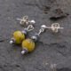 Yellow Turquoise and Hematite Sterling Silver dangles suspended from sterling silver stud ear posts with scroll backs, shown lying side by side on a dark grey rock