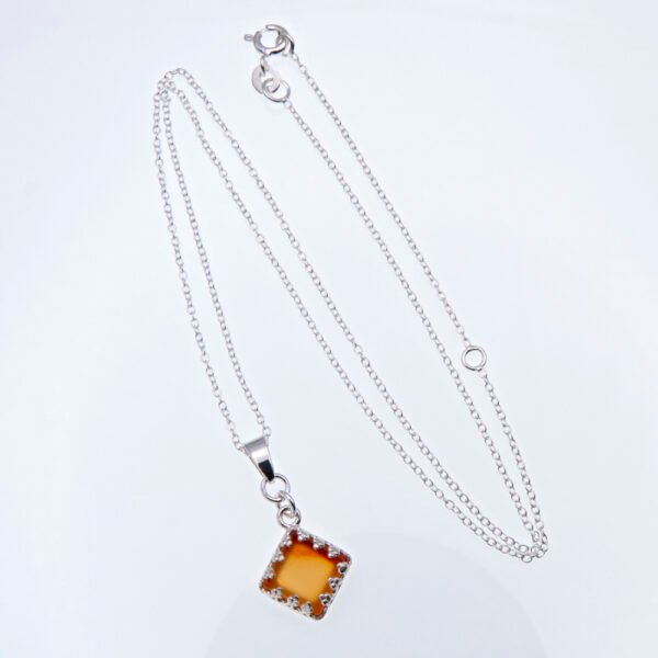 Carnelian Square Cabochon set in diamond shaped decorative Sterling Silver bezel pendant, suspended from a Sterling Silver chain, shown laid flat on a white surface
