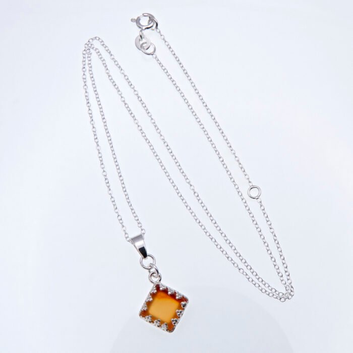 Carnelian Square Cabochon set in diamond shaped decorative Sterling Silver bezel pendant, suspended from a Sterling Silver chain, shown laid flat on a white surface