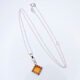 Carnelian Square Cabochon set in diamond shaped decorative Sterling Silver bezel pendant, suspended from a Sterling Silver chain, shown laid flat on a white surface