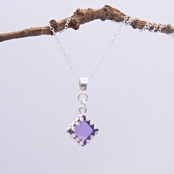 Amethyst square cabochon set in Sterling Silver diamond shaped decorative bezel and suspended via decorative bail from a Sterling Silver chain, pictured hanging from twig