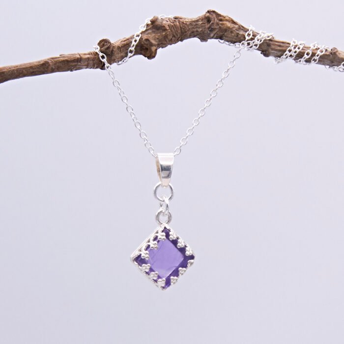 Amethyst square cabochon set in Sterling Silver diamond shaped decorative bezel and suspended via decorative bail from a Sterling Silver chain, pictured hanging from twig