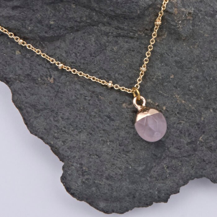 Rose Quartz Cabochon 24k gold plated silver pendant on gold plated satellite chain Rose Quartz Cabochon 24k Gold Plated Silver pendant on Gold Plated Satellite Chain close up view from above on dark grey stone