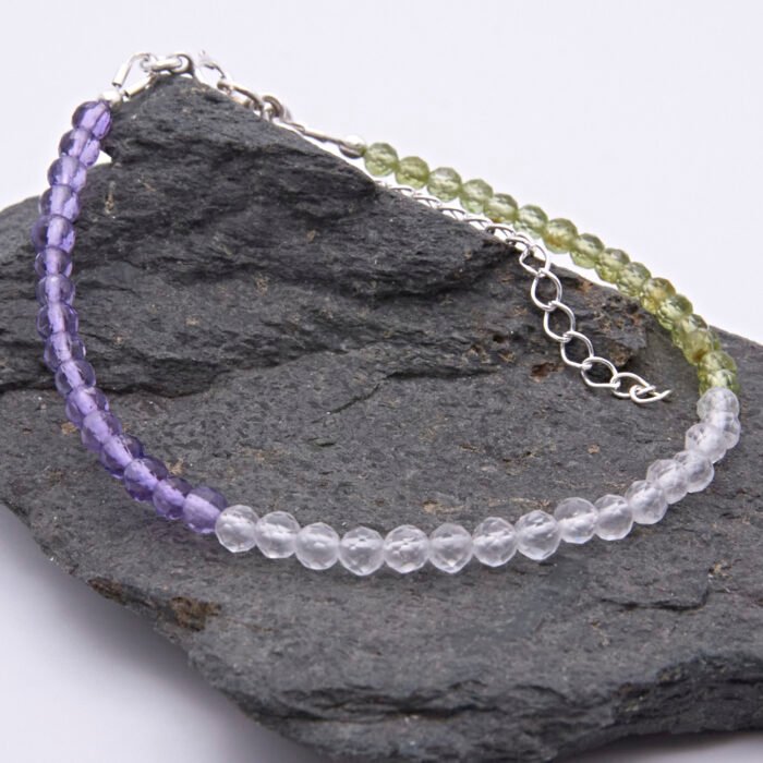Genderqueer Flag Colours Amethyst, Crystal Quartz and Peridot Gemstone Bracelet with Sterling Silver clasp and extender chain, shown from the side, laid on a dark grey stone