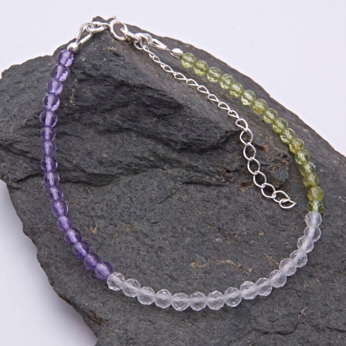 Genderqueer Flag Colours Gemstone Bracelet in Amethyst, Crystal Quartz and Peridot, with Sterling Silver clasp and extender chain, shown laid flat on a dark grey stone
