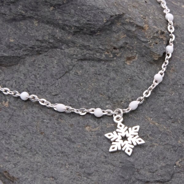 Sterling Silver and White Enamel Bead Bracelet with Sterling Silver Snowflake Charm shown laid flat on dark grey stone with close up of snowflake and part of chain