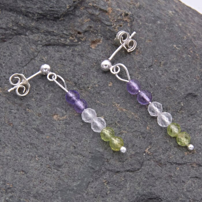Sterling Silver Stud Earrings with Mixed Gemstone Dangles in Amethyst, Crystal Quartz and Peridot shown laid flat on dark grey stone
