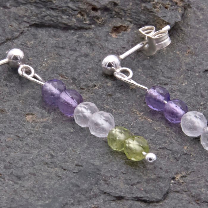Sterling Silver Stud Earrings with Mixed Gemstone Dangles in Amethyst, Crystal Quartz and Peridot shown close-up on dark grey stone