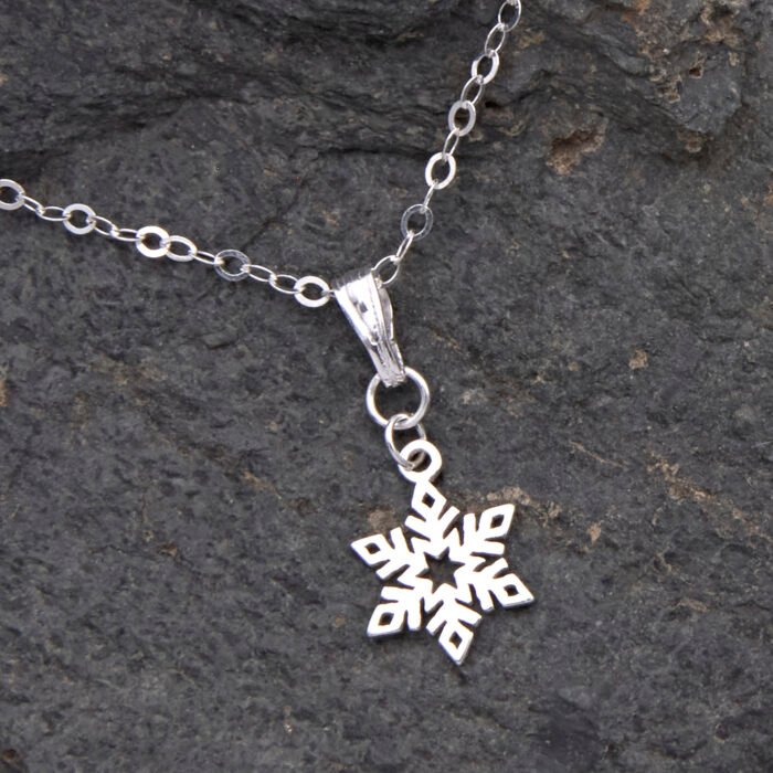 Sterling Silver Snowflake Charm Necklace, image shows close up of snowflake charm and bail on small area of chain, laid flat on dark grey stone