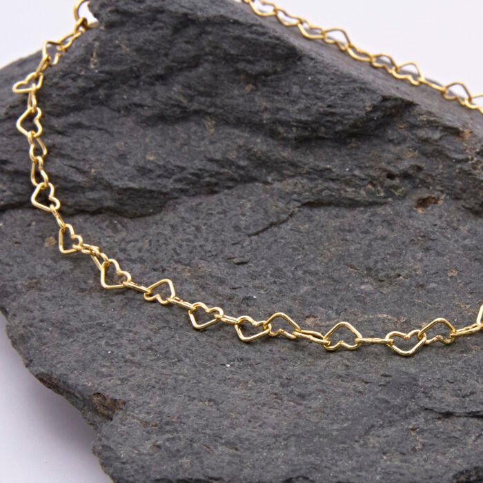 Gold Heart Link Chain Bracelet, close-up image of part of the chain, on dark grey stone