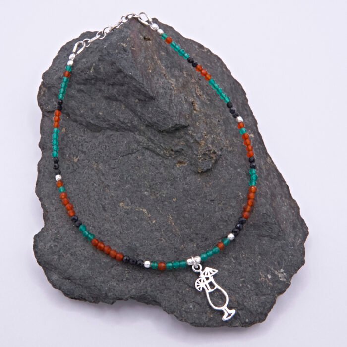Green Onyx, Carnelian and Sapphire Sterling Silver Bracelet with Sterling Silver Cocktail Charm in the centre, shown laid on a dark grey stone