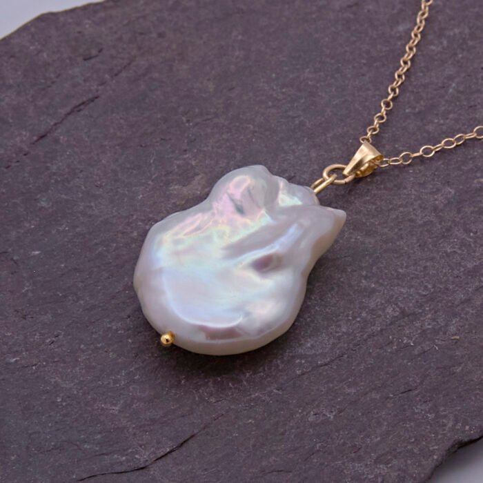 Baroque pear-shaped Freshwater Pearl Necklace, image shows close-up of pearl and part of chain on dark grey stone