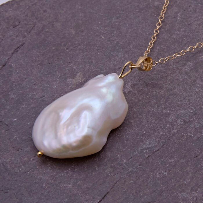 Baroque pear-shaped Freshwater Pearl Necklace, image is close-up of pearl and a little of the chain, shown on dark grey stone