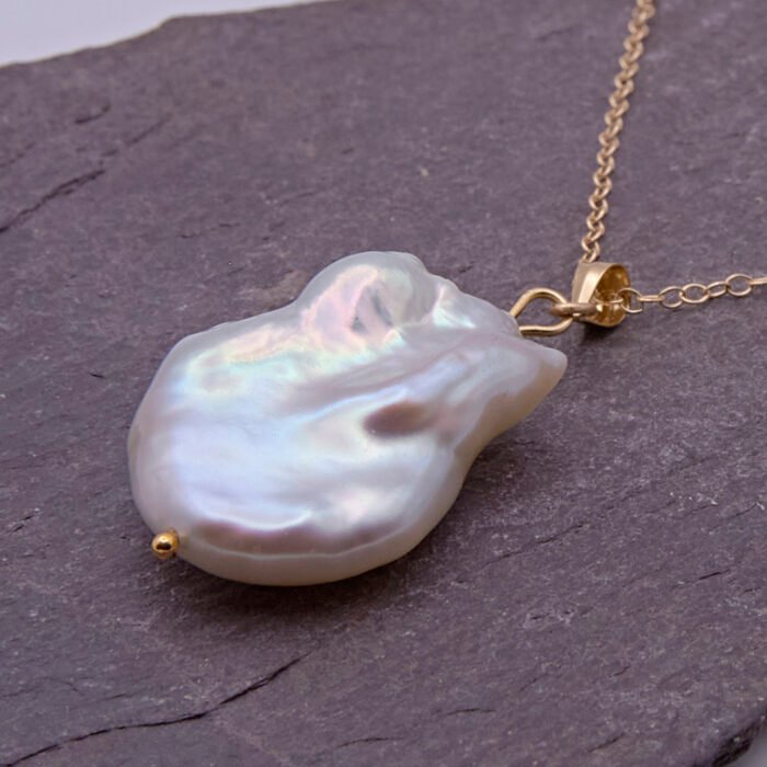 Baroque pear-shaped Freshwater Pearl Necklace, image shows close-up from the side of the pearl and part of the chain, on a dark grey stone
